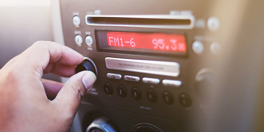 Ihminen vaihtaa radiokanavaa autossa.